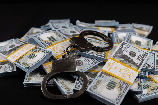 A million dollars in bundles lie on a black background and handcuffs on top. Big crime concept with money. Money on a black background with handcuffs..