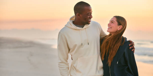 istock Casually Dressed Loving Young Couple Walking Along Beach Shoreline Hugging At Sunrise 2096225689