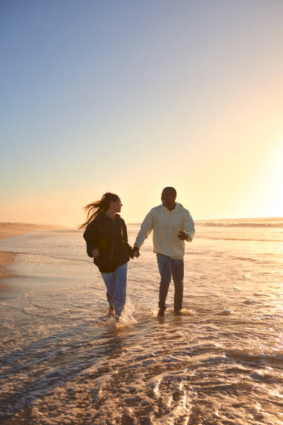 istock Casually Dressed Loving Young Couple Running Along Beach Shoreline Through Waves At Sunrise 2096238294