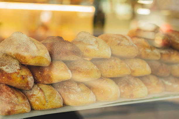 Stack of bread loaves are displayed in a window. The bread is white and he is freshly baked. Blurred view through store window
