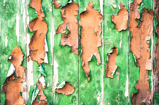 Close-up of wooden planks, painted long ago in green, then later in brown, with the paint peeling off with age.