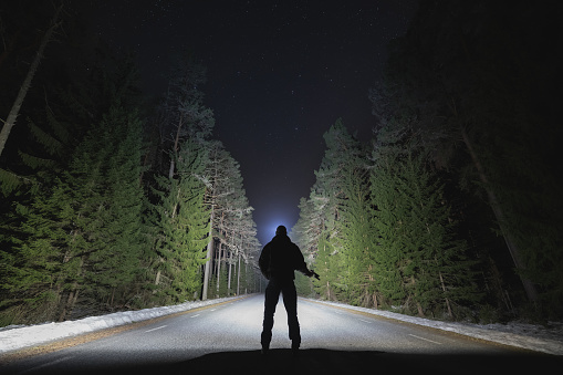 Silhouette of a man with a headlamp and a pistol in his hand on a forest road at night. High quality photo