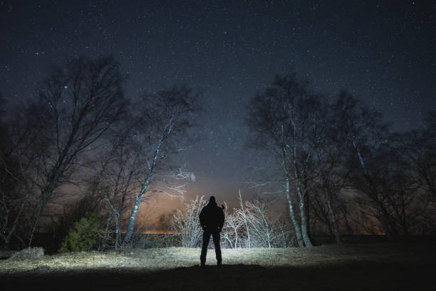 istock Silhouette of a man with a headlamp with a rifle behind his back in a night forest under a starry sky. 2096274714