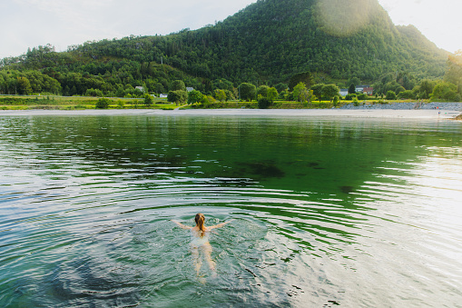 Smiling female with long hair swimming in the fjord with idyllic sunset Mountain View at the beautiful beach of in Møre og Romsdal, Scandinavia