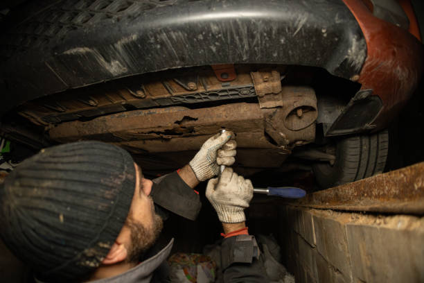 A man unscrews the nuts under the engine oil change machine in his garage. A man's gloved hands are repairing a car. In a garage near the house, a man is repairing a car.