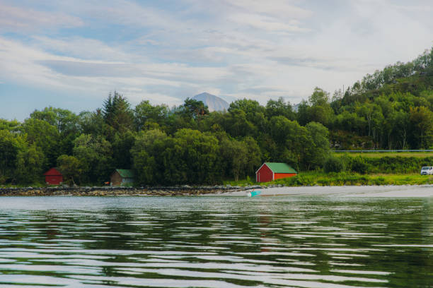 View if unrecognisable person holding turqouise paddle board at the beautiful beach with Mountain View in rural place if Norway