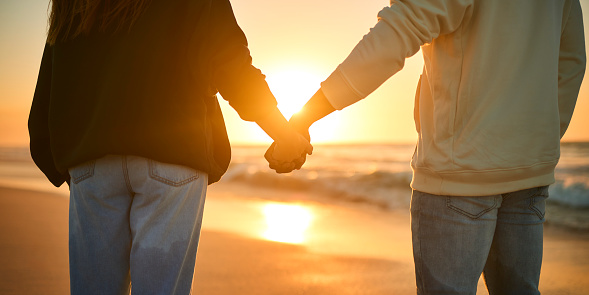 Close Up Of Casually Dressed Loving Young Couple Holding Hands On Beach Shoreline At Sunrise