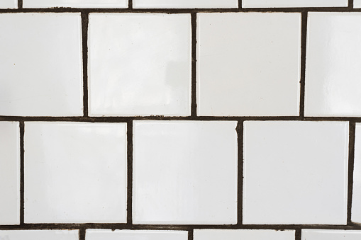 Old white ceramic wall tile pattern for decoration. Close-up vintage wall with bathroom ceramic white square tiles with defects fading.
