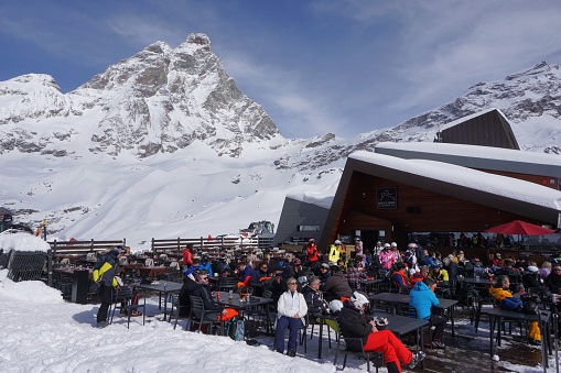 Cervinia, Italy - 11 March 2024: Skiers are relaxing at a cafe near the Plan Maison lift station in the Cervinia ski area, with the Matterhorn in the background.