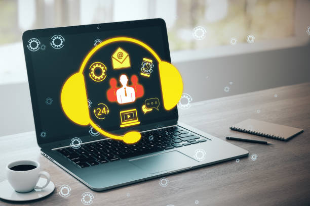 istock Close up of laptop and coffee cup on office desk with creative customer support icon on blurry background. Hotline concept. 2096320284