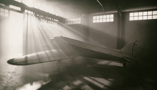 Light streams through windows of an old-style aircraft hangar to reveal the icons form of a DC-3 Dakota aeroplane. Model photography.