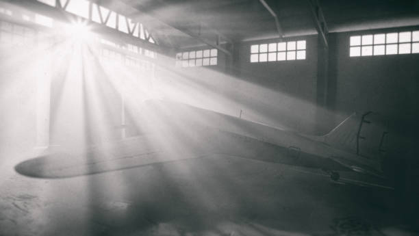 Light streams through windows of an old-style aircraft hangar to reveal the icons form of a DC-3 Dakota aeroplane. Model photography.