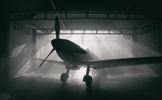 Sunlight streams through windows and reveals the iconic Supermarine Spitfire, seen here sitting in a traditional old aircraft hangar from WWII. Scale model photography.