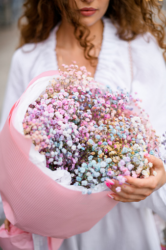 Tenderness bouquet of soft pink, lilac, lavender, blue small flowers in the hands. Hidden face of a young girl who stands on a street