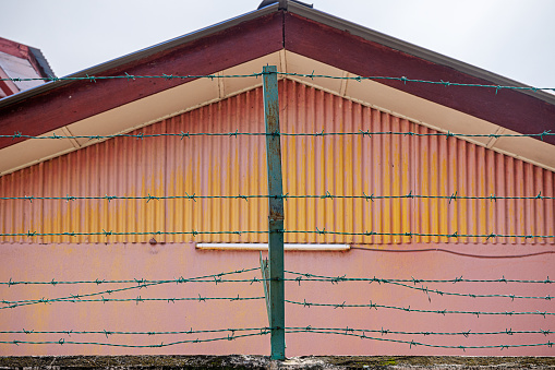 Triangular gable with corrugated iron plates and a neon tube behind barbed wire in the Malaysian capital Kuala Lumpur