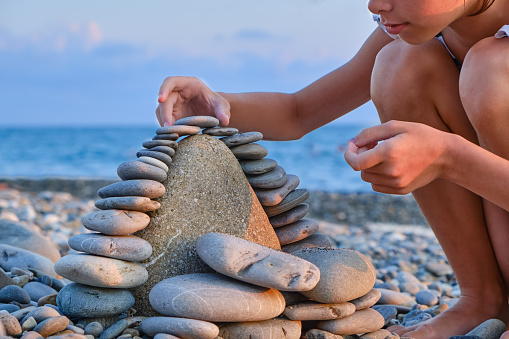 The child's hands lay pebbles, stones in a tower on the beach in summer, close-up