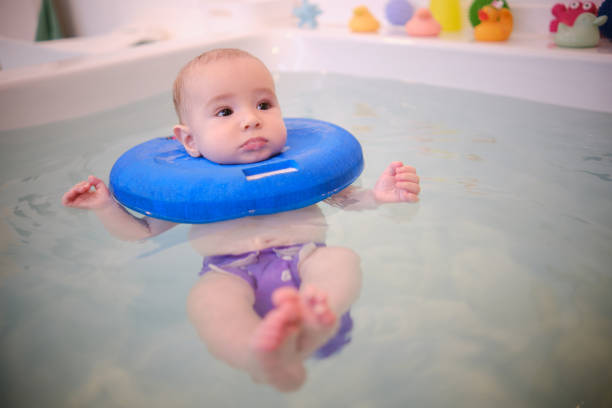 A baby wearing a blue swimming cap is in a bathtub