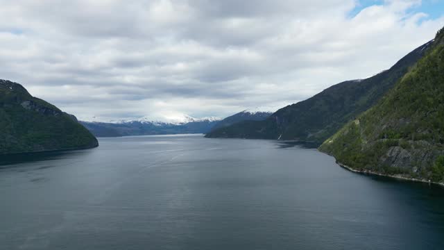 Nordalsfjorden in Fjord, Norway with snowy mountain tops, green forests, car ferries on a cloudy day