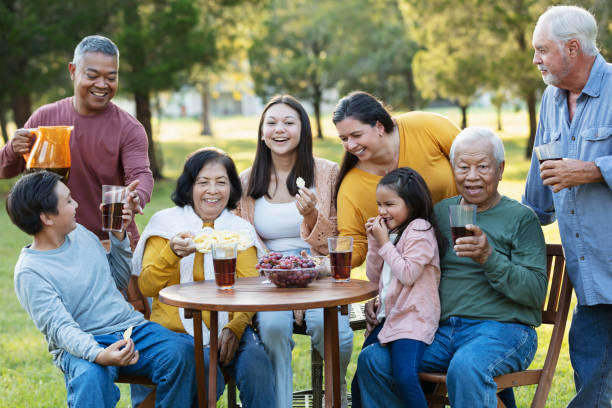 multi-generation multiracial family eating in back yard - filipino ethnicity grandfather senior adult family - fotografias e filmes do acervo