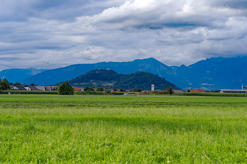 Scenic view of rural landscape with village Spodnje Bitnje and church tower in the background on a cloudy summer day. Photo taken August 10th, 2023, Žabnica, Slovenia.