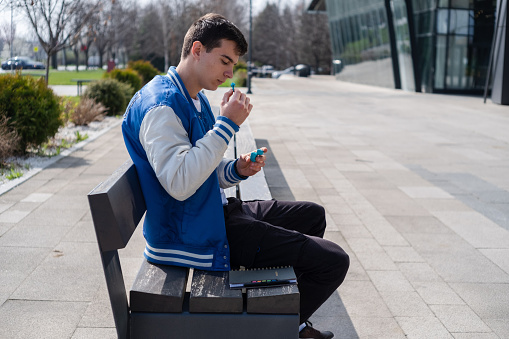 Young student listening to music on earbuds by the modern building.