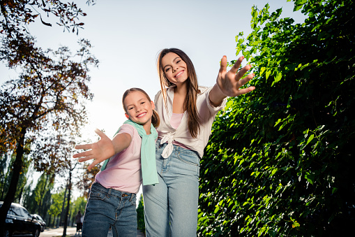 Portrait of two cheerful cute sisters toothy smile raise opened hands welcome you pastime walk downtown outdoors.