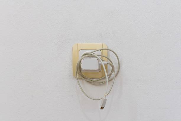 The phone charger is plugged into the electrical power socket on wall when not in use. Leaving the phone charger plugged in. Wasting energy.