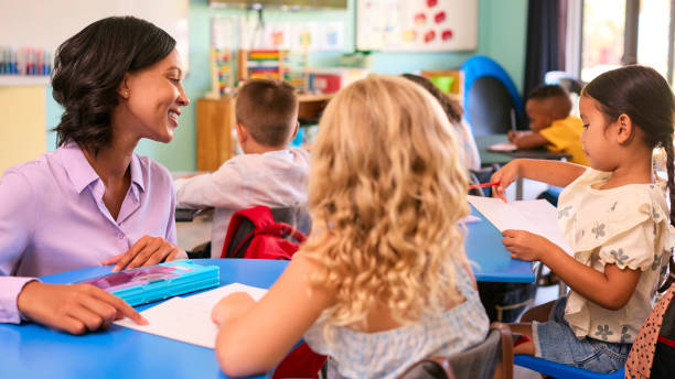 istock Female Primary Or Elementary School Teacher Helping Students At Desks In Multi-Cultural Class 2096483577