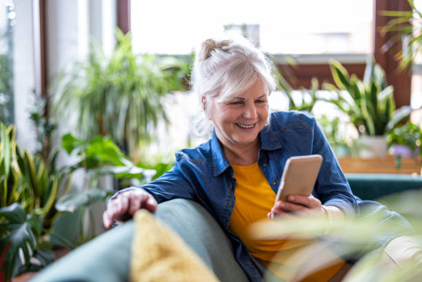 istock Smiling senior woman using smart phone while sitting on sofa at home 2096495176