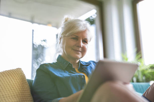 istock Mature woman using digital tablet while sitting on sofa at home 2096495200