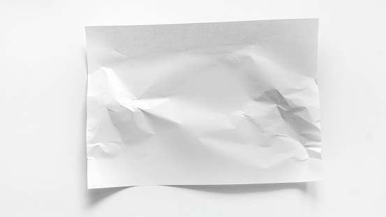 A white slightly crumpled A4 sheet lies on a white background. Mockup for inscriptions, words, advertisements with copy space. White crumpled sheet of paper close-up.