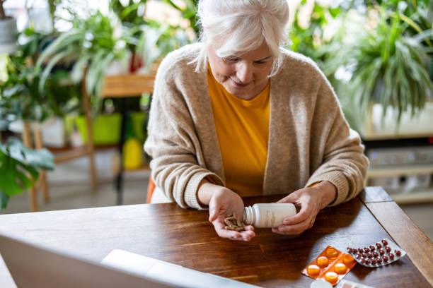istock Senior woman taking pills from a bottle while sitting at the table at home 2096498487