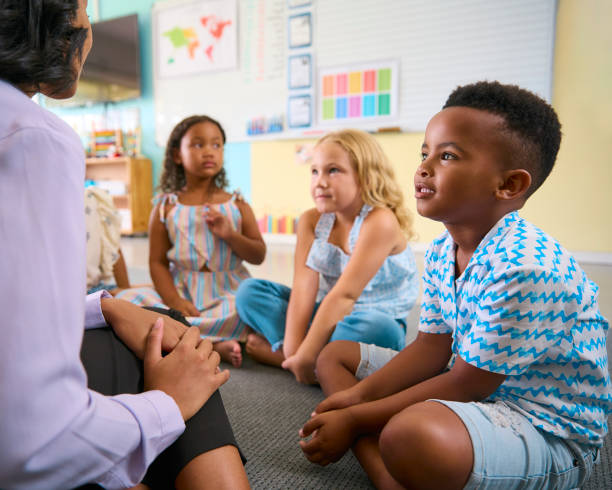 istock Multi-Cultural Primary Or Elementary School Class Sitting On Floor Listening To Teacher In Classroom 2096503229