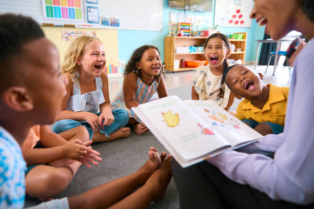 Female Primary Or Elementary School Teacher Reads Story To Multi-Cultural Class Seated In Classroom - foto stock