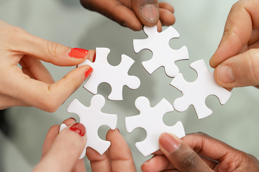 Multi-ethnic hands - assembling puzzle - symbol of teamwork and solutions, collaboration and problem solving - finding common solution concept