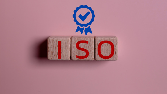 ISO on wooden cubes with guarantee icon on pink background. ISO quality control certification approval concept.