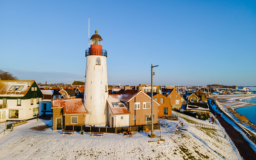 The Dutch village of Urk in Flevoland Netherlands with its old harbor and iconic lighthouse during winter with snow and a blue sky