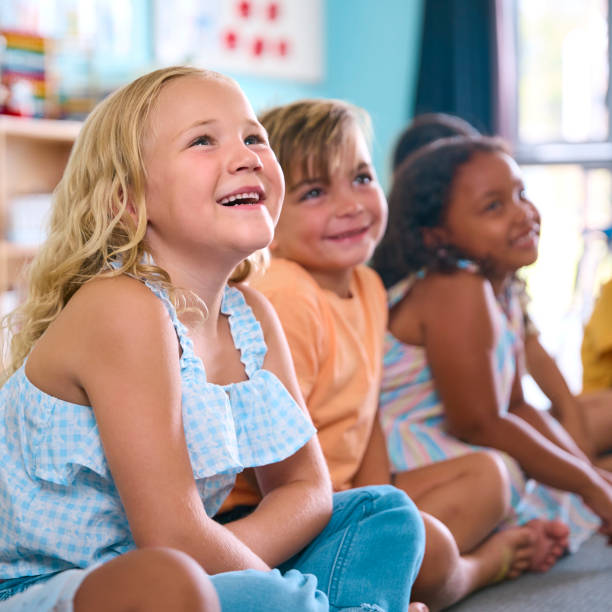 istock Line Of Smiling Primary Or Elementary School Students Sitting On Floor During Classroom Lesson 2096534244