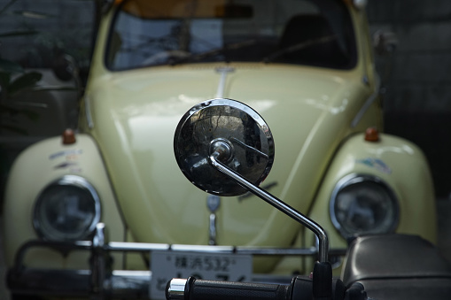 Scenery of a German retro beetle seen through the rear view mirror of a Japanese retro motorcycle found in Japan's ancient capital Kamakura, photographed data March 2024, Kanagawa Prefecture, Kamakura City, Japan.