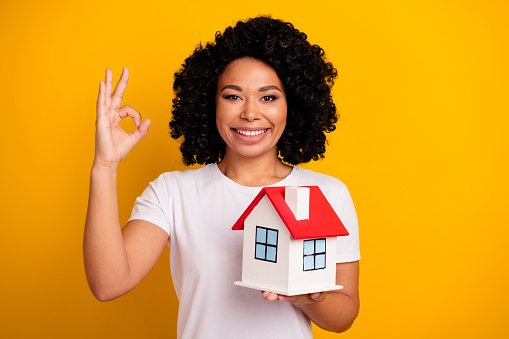 Photo of attractive mixed-race woman dressed white t-shirt hold house show okey recommend real estate isolated on yellow color background.