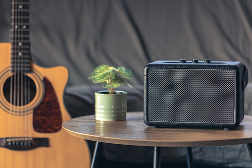 Close up, portable music speaker and acoustic guitar in the interior of the room. Audio equipment and digital device.