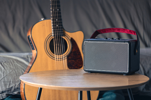 Close up, portable music speaker and acoustic guitar in the interior of the room. Audio equipment and digital device.