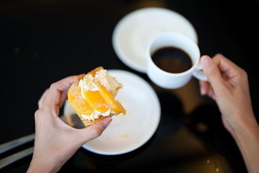 An overhead view of a woman enjoying a peach strudel paired with a cup of rich black coffee makes for a perfect post-meal treat at a cozy cafe