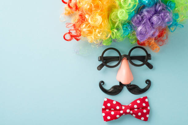istock April 1st hoax scene: top view snapshot with jesting spectacles, clown's locks, bow tie, faux mustaches, and make-believe nose, laid out to simulate visage on light blue backdrop, space for commentary 2096635215