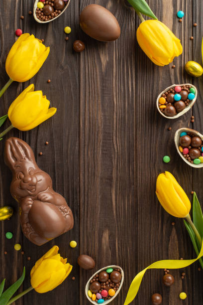 istock Easter delight concept: Overhead vertical shot of broken chocolate eggs revealing vibrant sweets, a chocolate rabbit, and fresh tulips on a wood surface, with space for text 2096635227