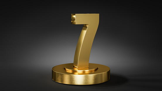 The number 7 on a pedestal / podium in golden color in front of dark background with spot light.