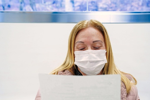 A woman wearing a mask reading a health document in waiting room of a hospital. Health day