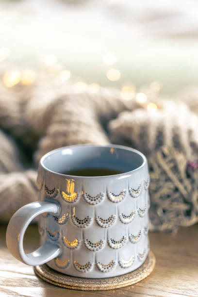 Close-up, shiny gray cup on a blurred background with a knitted element. Home composition with a cup of hot drink.