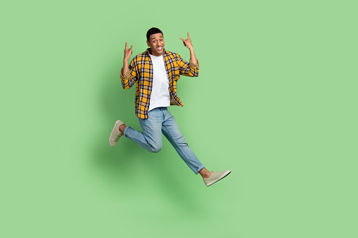 Full size portrait of carefree active sporty guy jump demonstrate heave metal symbol empty space isolated on green color background.