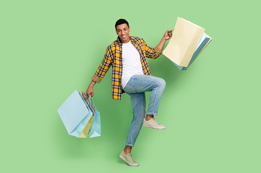 Full body portrait of overjoyed positive person hold store bags special sale offer isolated on green color background.